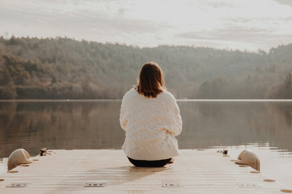 Woman sitting on a dock, reflecting by a serene lake.