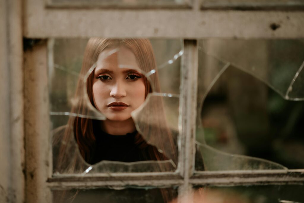 Woman standing behind a broken window, symbolizing emotional struggles and the strength needed for healing from a narcissistic mother by setting boundaries.