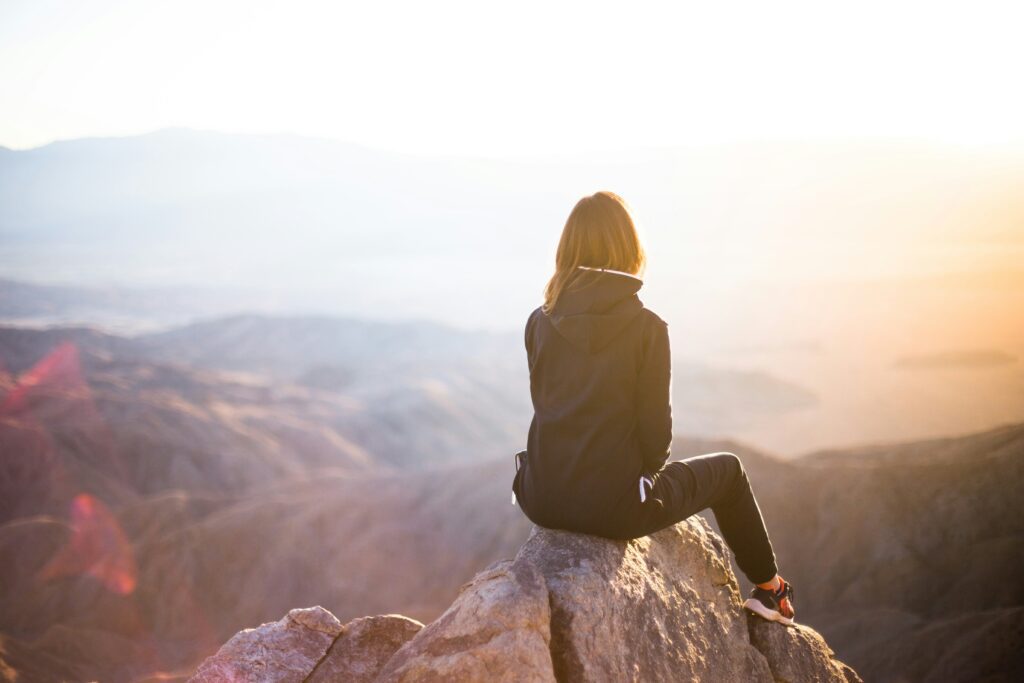 Woman sitting on a mountain peak, gazing at a serene landscape, symbolizing managing emotions with a narcissistic mother and finding clarity and control.