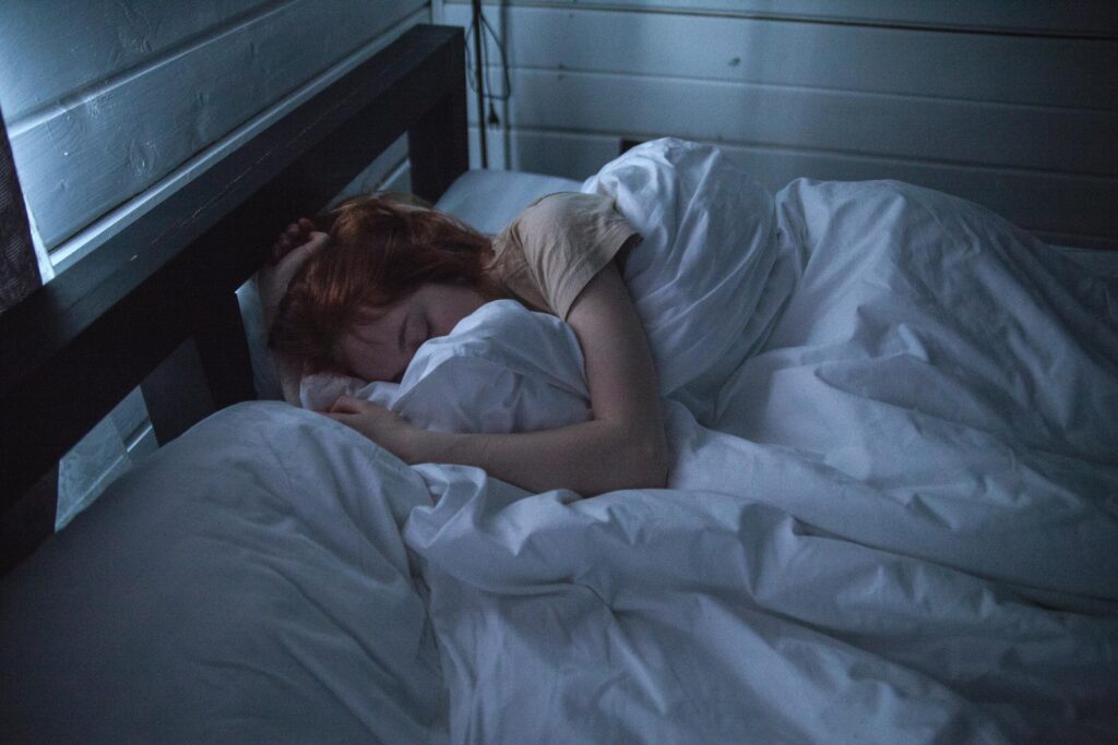 Woman lying in bed, curled under a blanket, reflecting the emotional struggle of managing emotions with a narcissistic mother.