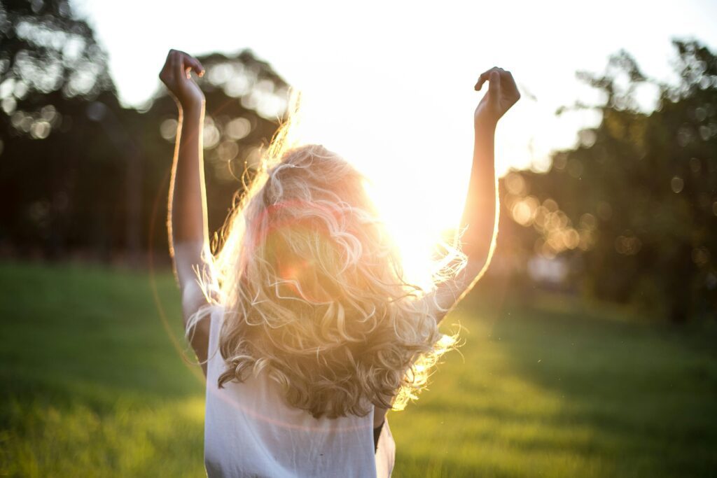 A woman standing in a field with her arms raised in sunlight, symbolizing freedom and peace after realizing narcissistic abuse as an adult.